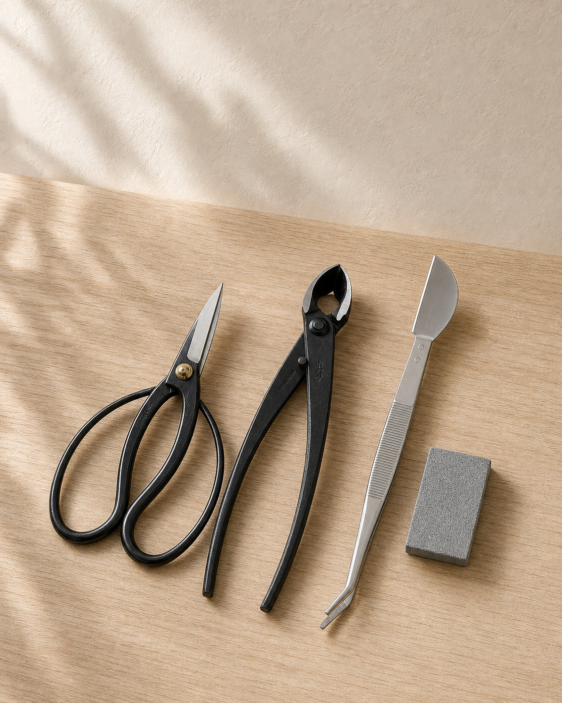 Wazakura Japanese bonsai tool kit with black butterfly scissors, concave cutter, stainless tweezers and a grey sap eraser on pale oak